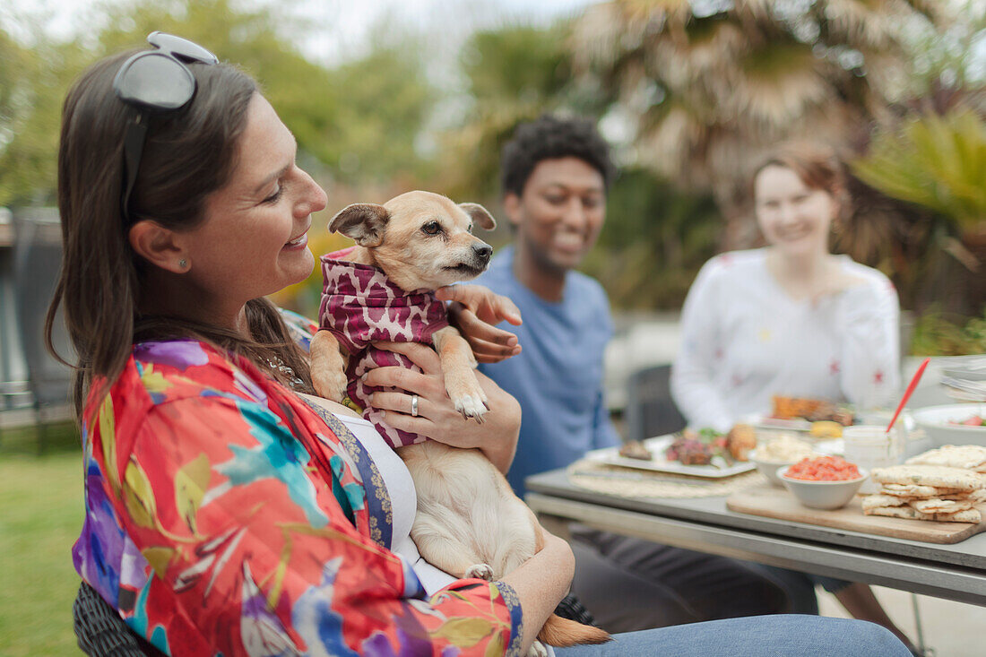 Happy woman holding cute dog at patio table