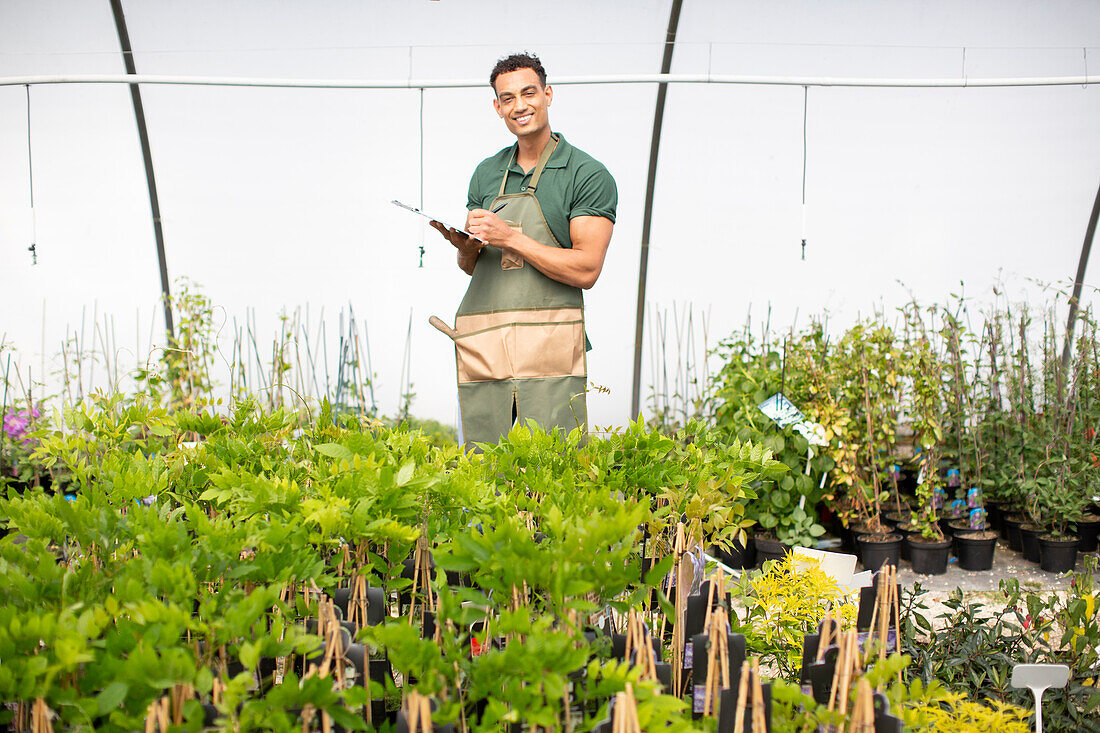 Happy male plant nursery owner in apron in greenhouse