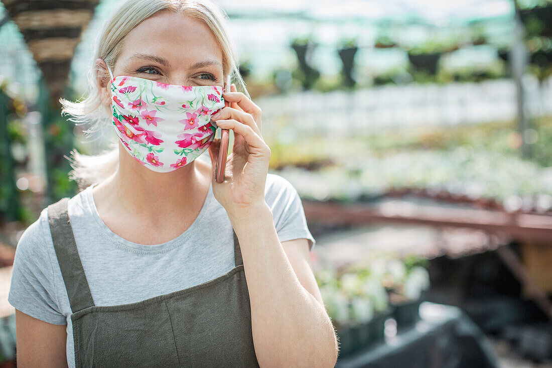 Female garden shop owner in face mask talking on smart phone