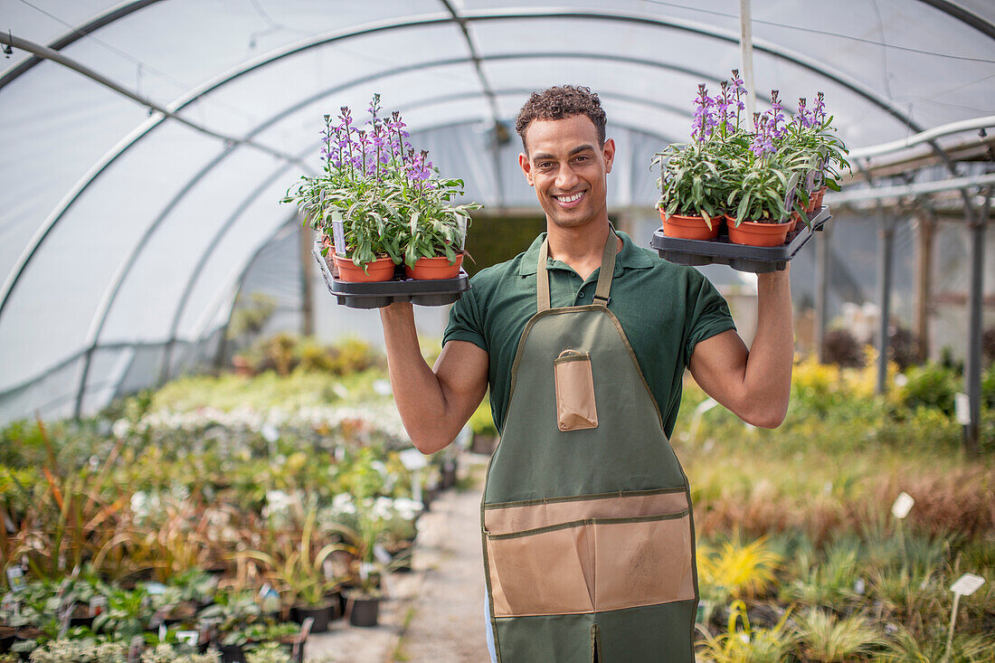Smiling male plant nursery worker with flowers in greenhouse