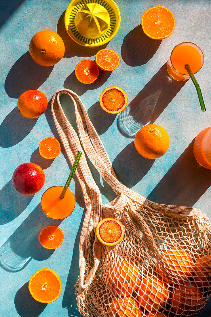 Einkaufsnetz mit Orangen, Saftpresse und frisch gepresster Orangensaft in Gläsern