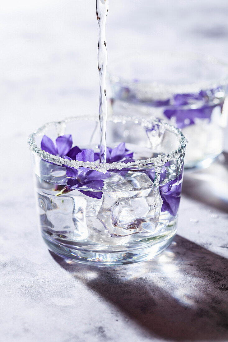 Water with ice and flowers in a glass with sugar rim