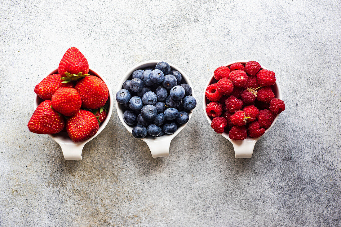 Erdbeeren, Heidelbeeren und Himbeeren in Schälchen auf Betonuntergrund