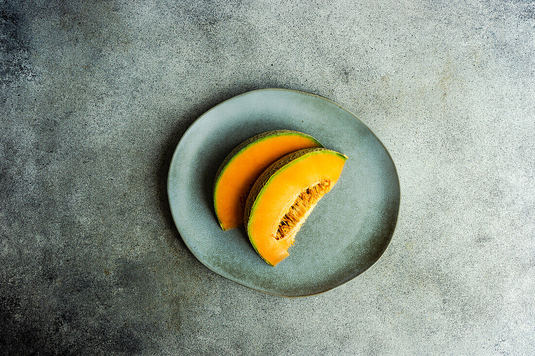 Slies of ripe cantaloupe melon on the bright ceramic plate on the concrete table