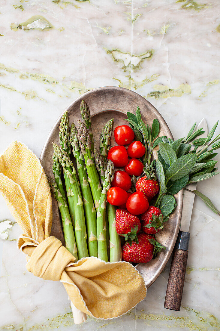 Green asparagus, tomatoes, strawberries, and sage on a silver tray