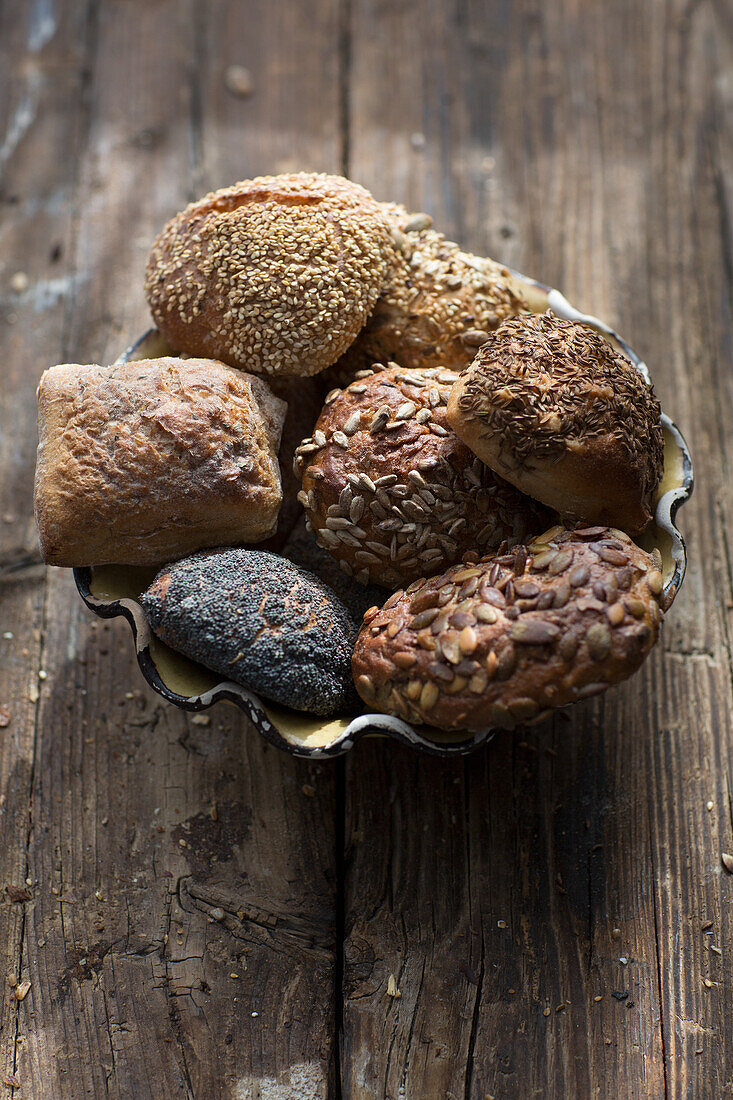 Assorted grain rolls in a bowl on a wooden base