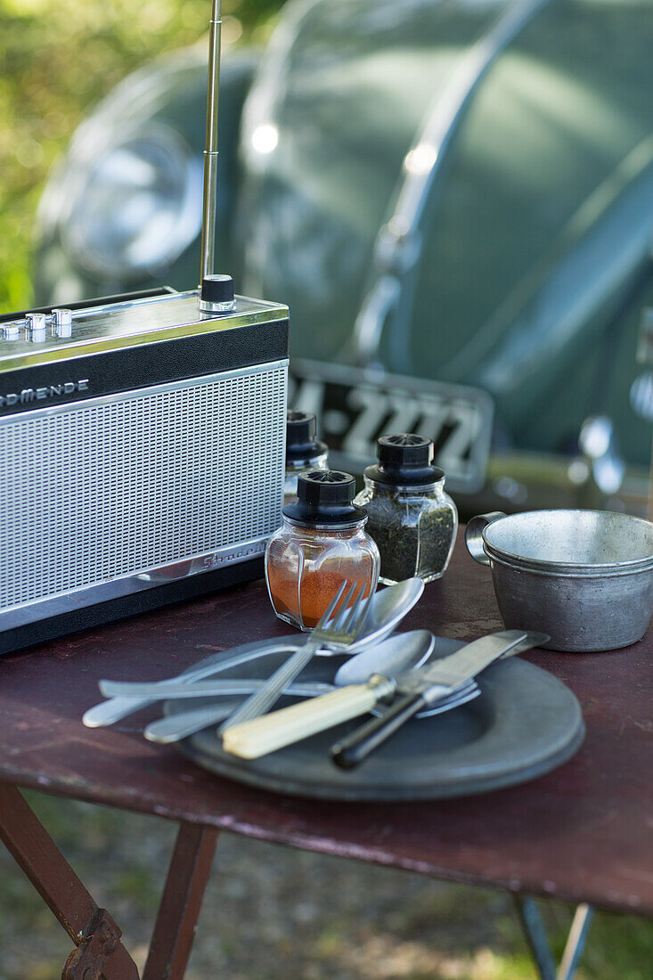 Gedeckter Campingtisch mit Kofferradio, Gewürzstreuern, Tellern und Besteck
