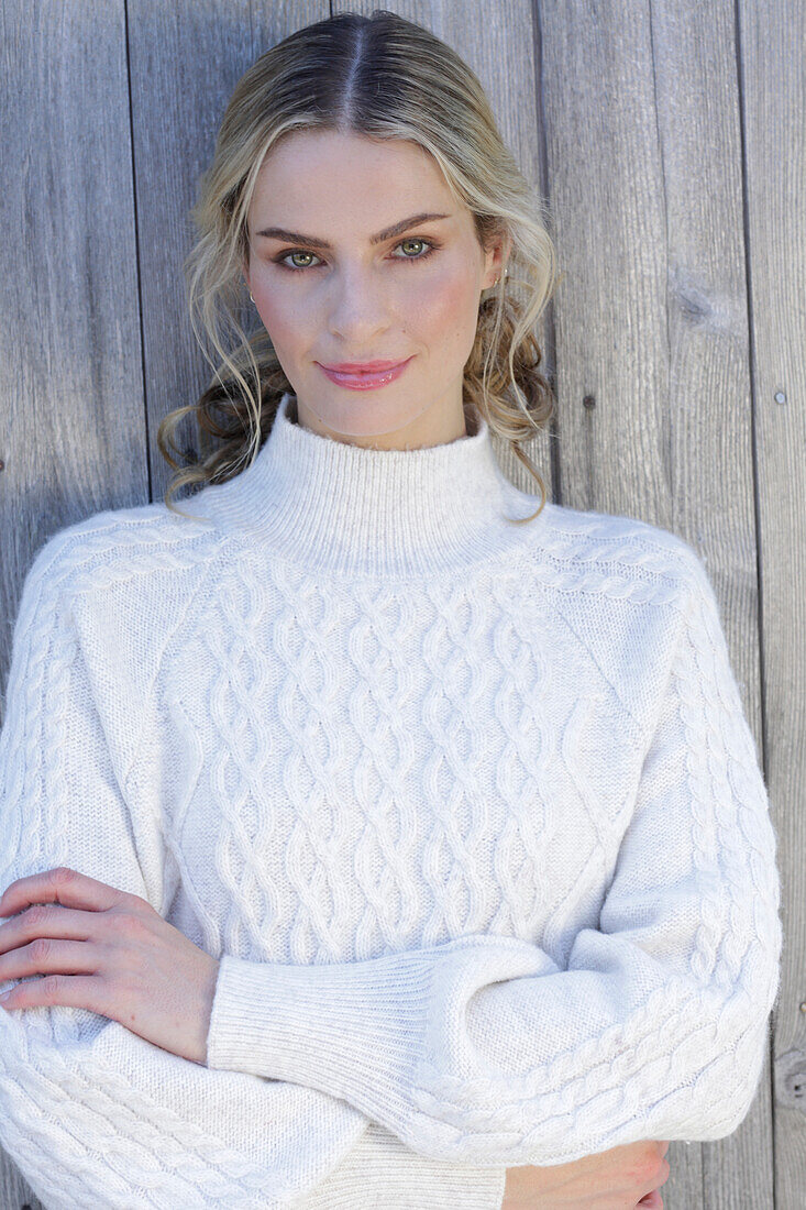 Young blond woman in white knitted jumper in front of board wall