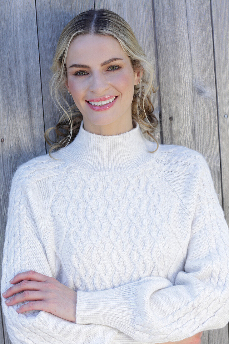 Young blond woman in white knitted jumper in front of board wall