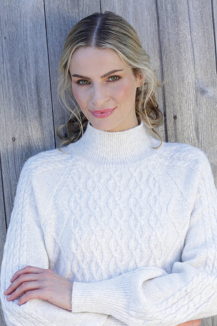 Young blond woman in white knitted jumper in front of board wall