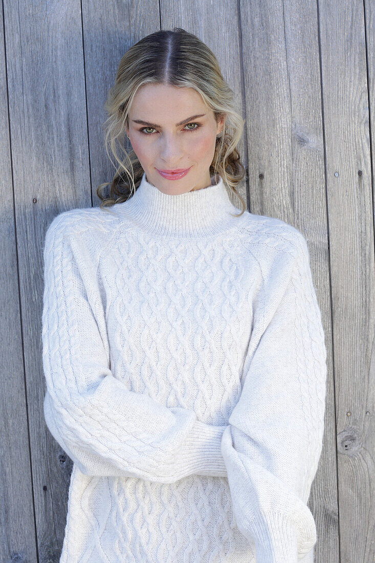 Young blond woman in white knitted jumper in front of board wall