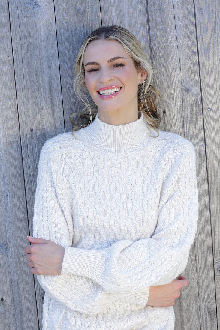 Young blond woman in white knitted jumper in front of board wall