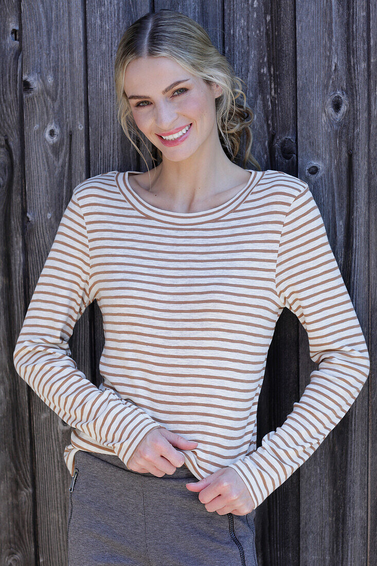 Young blond woman in striped shirt in front of board wall