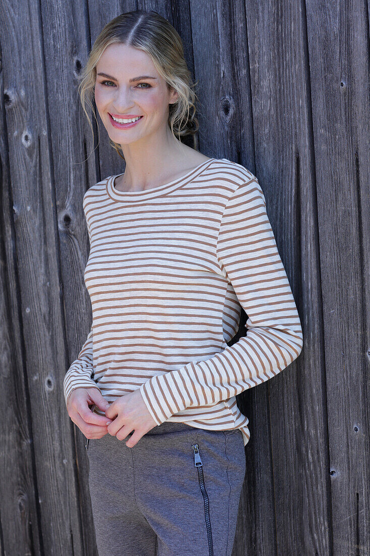 Young blond woman in striped shirt in front of board wall