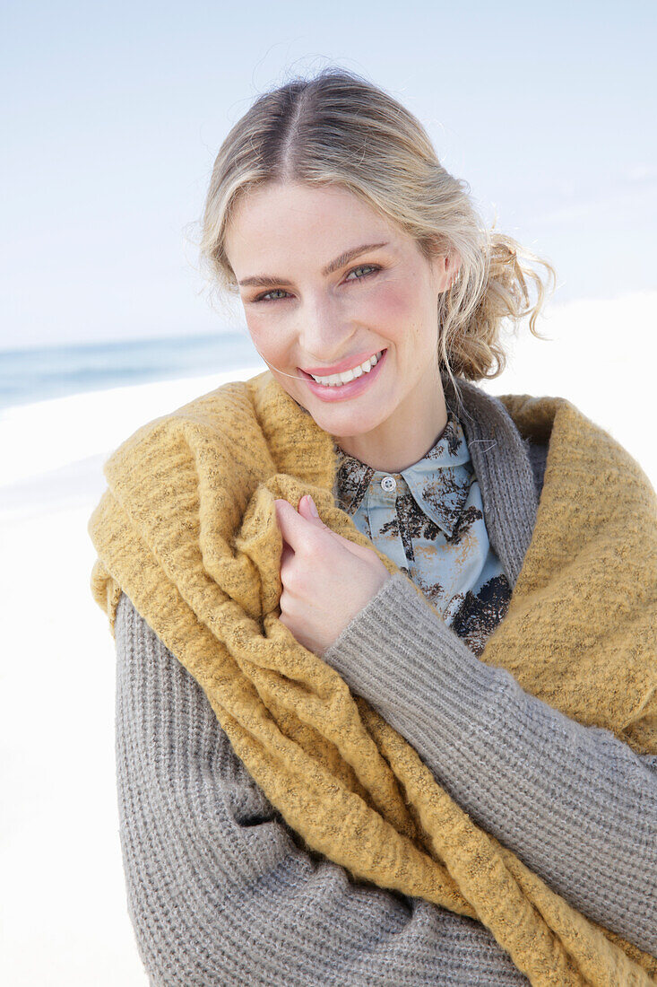Junge blonde Frau mit gelbem Schal in grauer Strickjacke am Strand