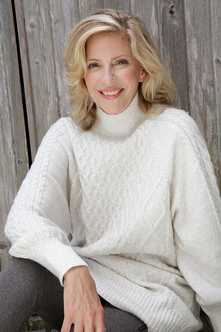 Reife blonde Frau in weißem Strickpullover und grauen Leggins