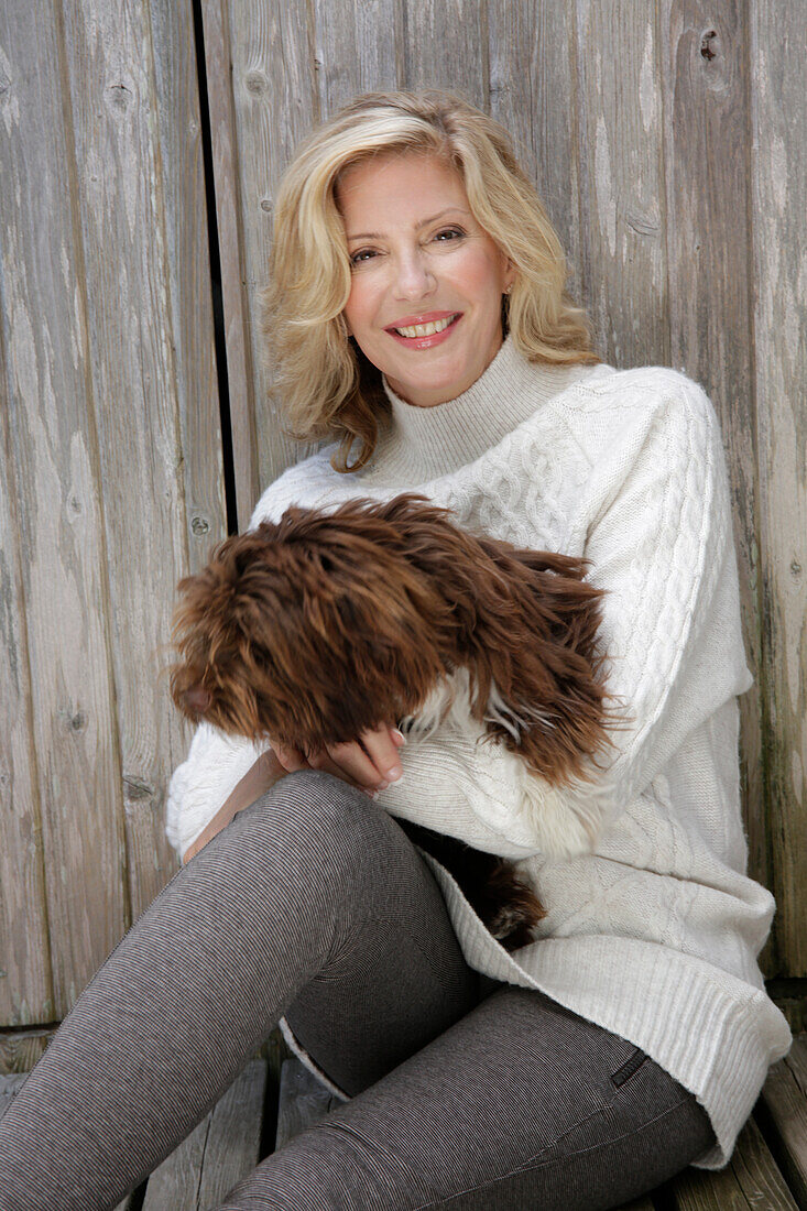 Reife blonde Frau mit Hund in weißem Strickpullover und grauen Leggins