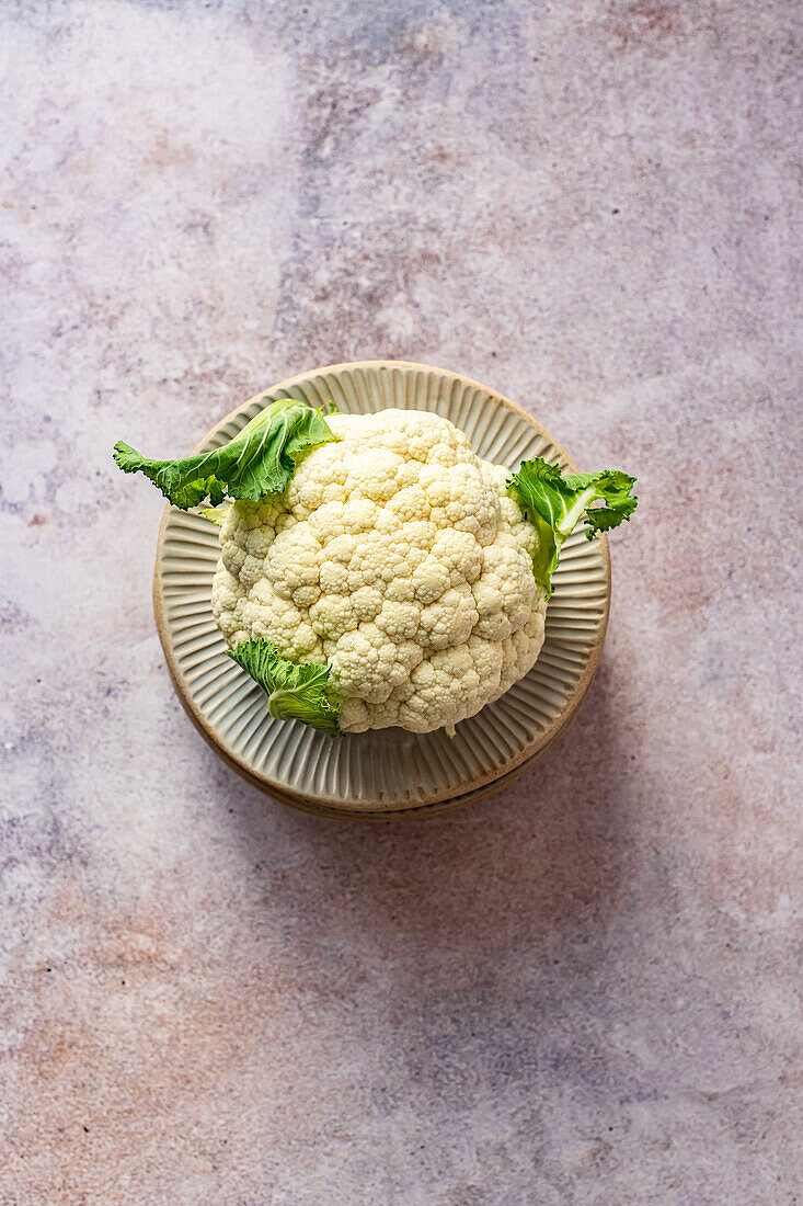 Organic cauliflower with leaves on a stack of fluted ceramic plates