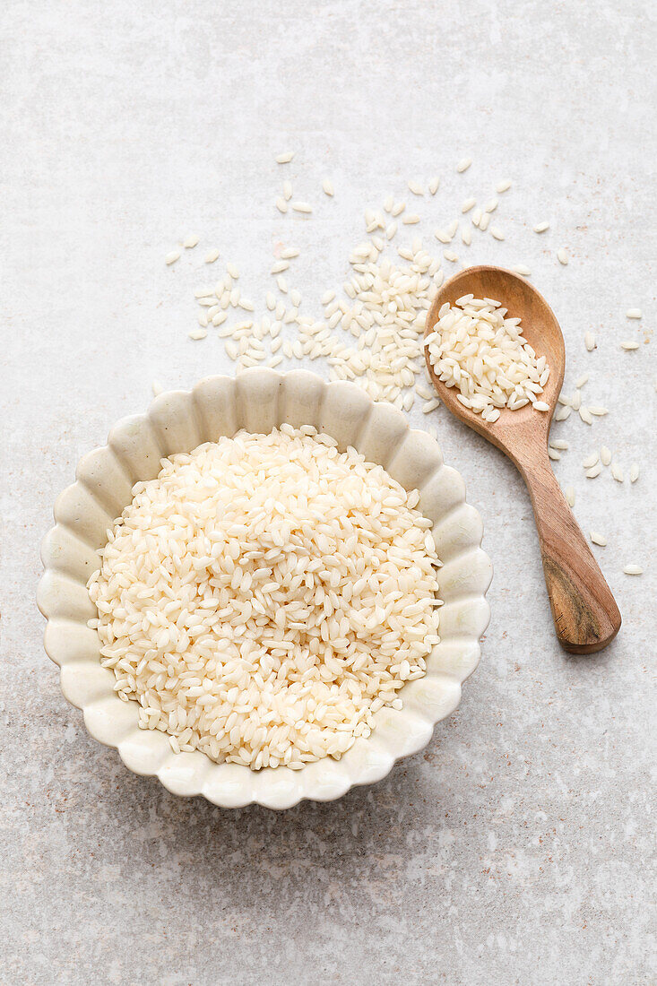 Arborio rice in a small bowl and on a wooden spoon