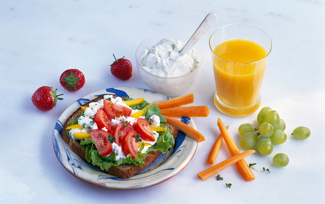 Wholemeal bread with lettuce, cottage cheese, tomato, and peppers served with a glass of orange juice