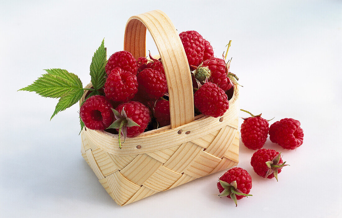 Raspberries in a small basket on a light background