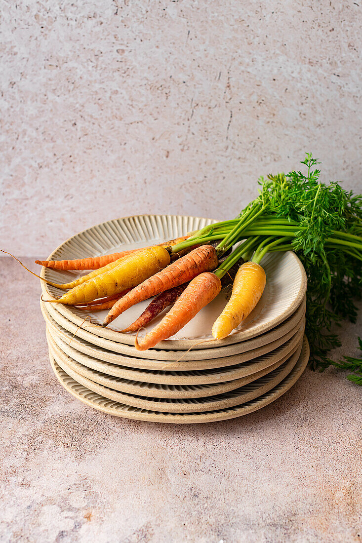 A bunch of colourful organic carrots with greens on a stack of handmade ceramic plates