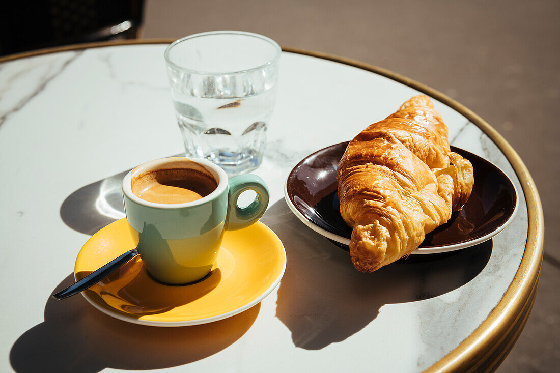Croissant, Espresso und ein Glas Wasser auf Bistrotisch