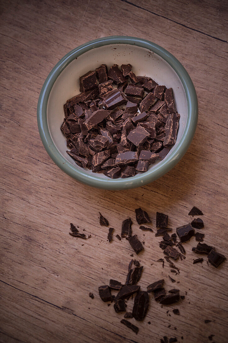 Dunkle Schokolade in Stücke gehackt in Schälchen und auf Holzuntergrund