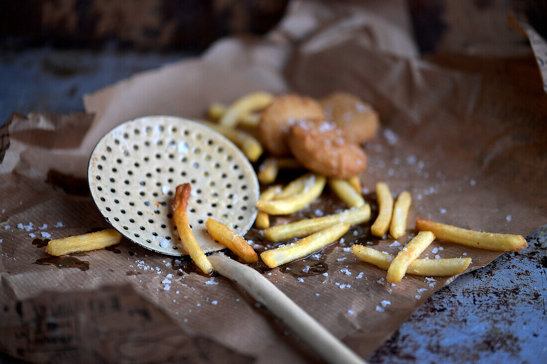 Pommes Frites mit Sieblöffel auf Papier