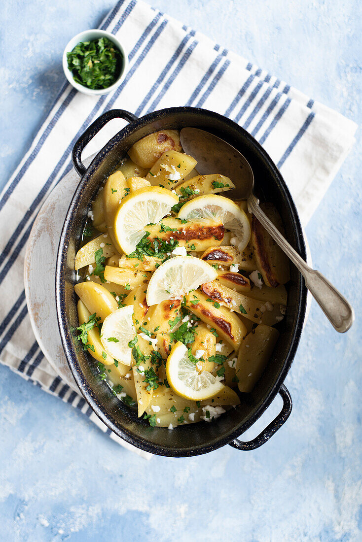 Oven baked potatoes with garlic and lemon, served with fresh parsley and feta cheese