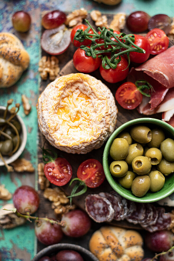 Snack board with cheese, jamon serrano, fuet, buns, olives, cherry toamtoes, grapes, walnuts and capers