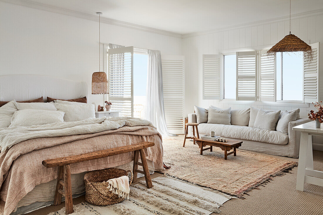 Doppelbett mit Vintage-Leinenbettwäsche, Fensterläden, weißes Leinensofa und Rattanleuchten im Schlafzimmer