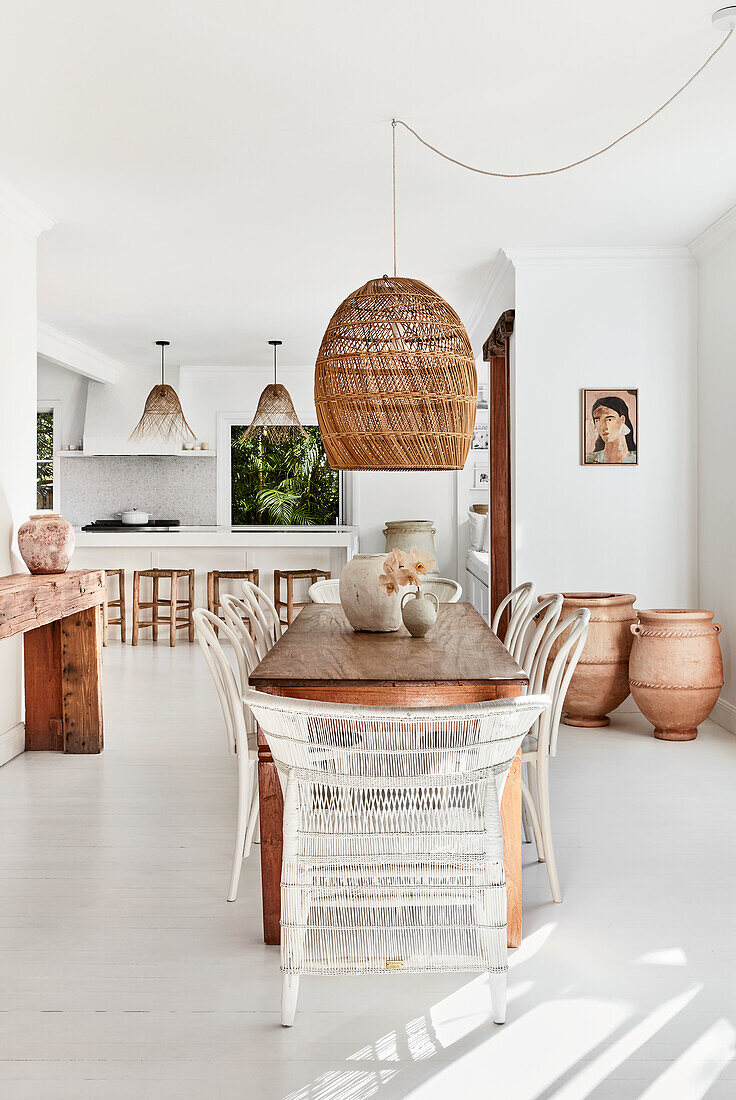 Rustic wooden dining table with white chairs, rattan lamp above in open living area