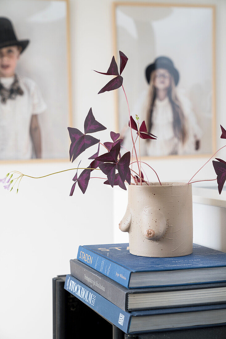 Hand-painted vase with leafy branches on a stack of books, children's portraits in the background