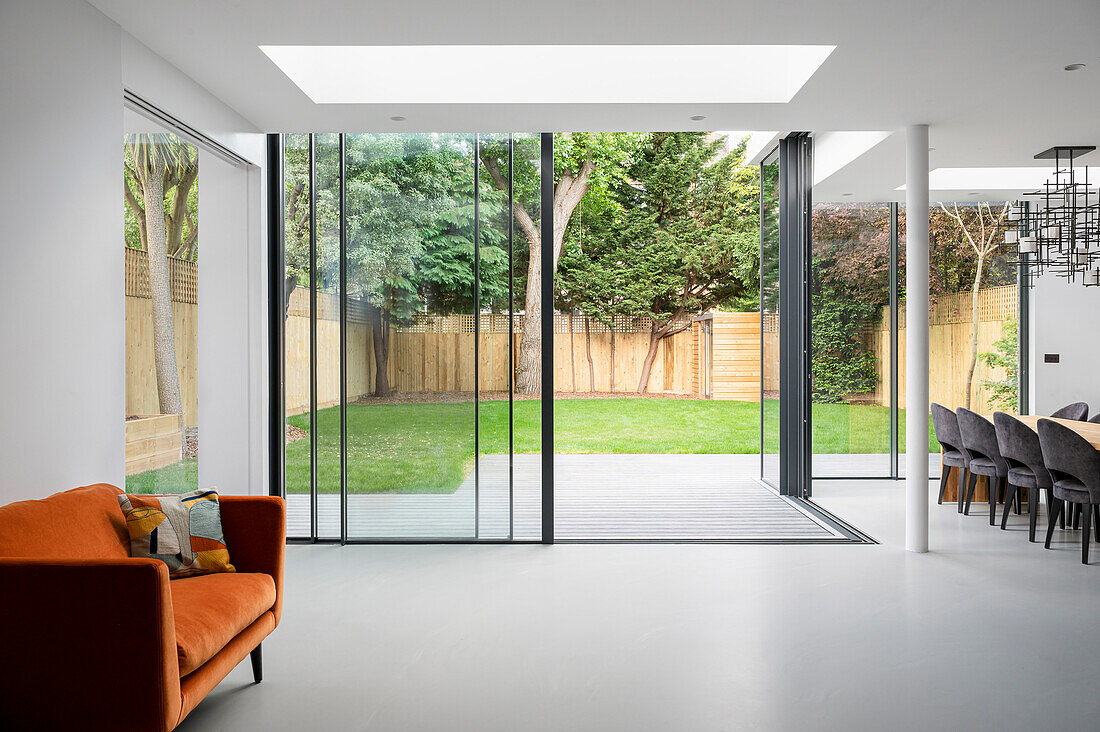 Orange sofa in open living room, view through glazing into the garden