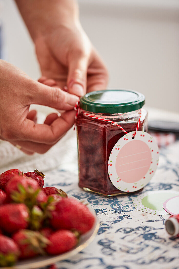 Tying a gift tag around a glass with homemade strawberry jam
