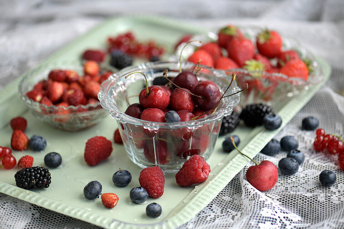 Sommerbeeren und Kirschen in Glasschalen auf Tablett