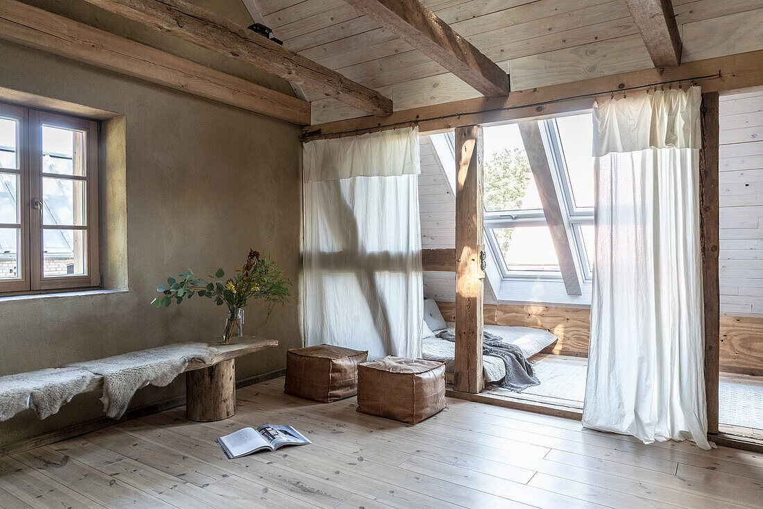 Wooden bench with sheepskin throw as a table and leather square pouf, sleeping area with pitched roof in an old country house