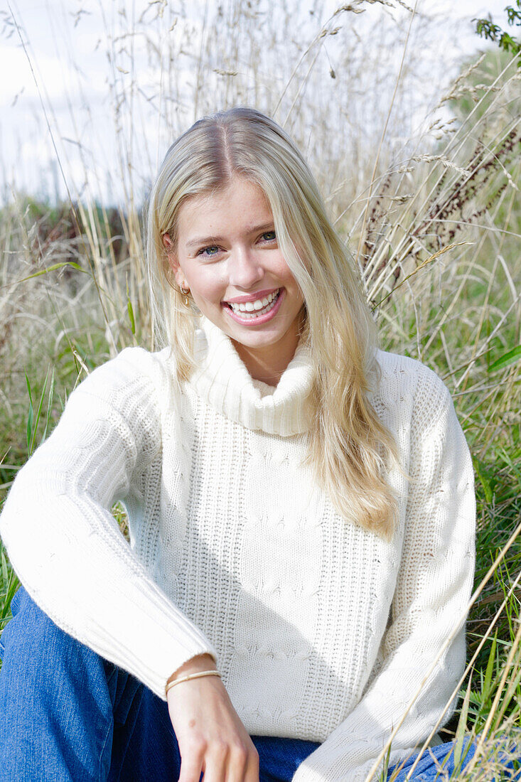 Junge blonde Frau in weißem Rollkragenpullover und Jeans in der Natur