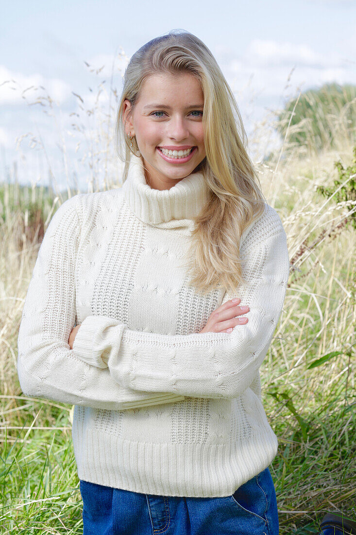 Junge blonde Frau in weißem Rollkragenpullover und Jeans in der Natur