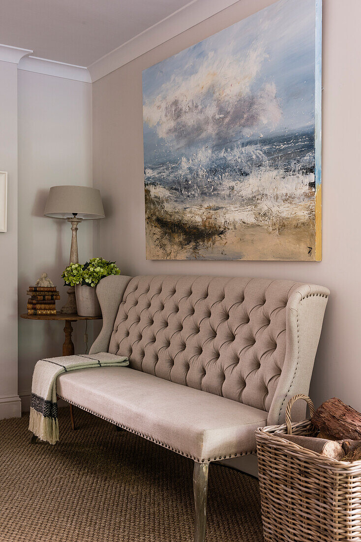 Cream colored, capitone sofa with high backrest under large oil painting