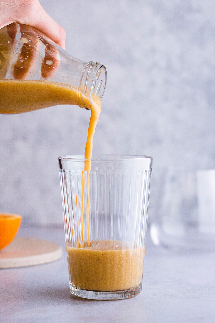 Orangen-Smoothie fürs Frühstück in ein Glas einschenken