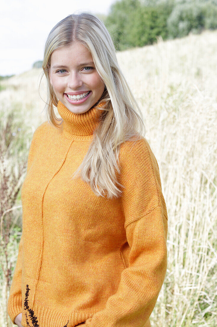 Junge blonde Frau in gelbem Rollkragenpullover in der Natur