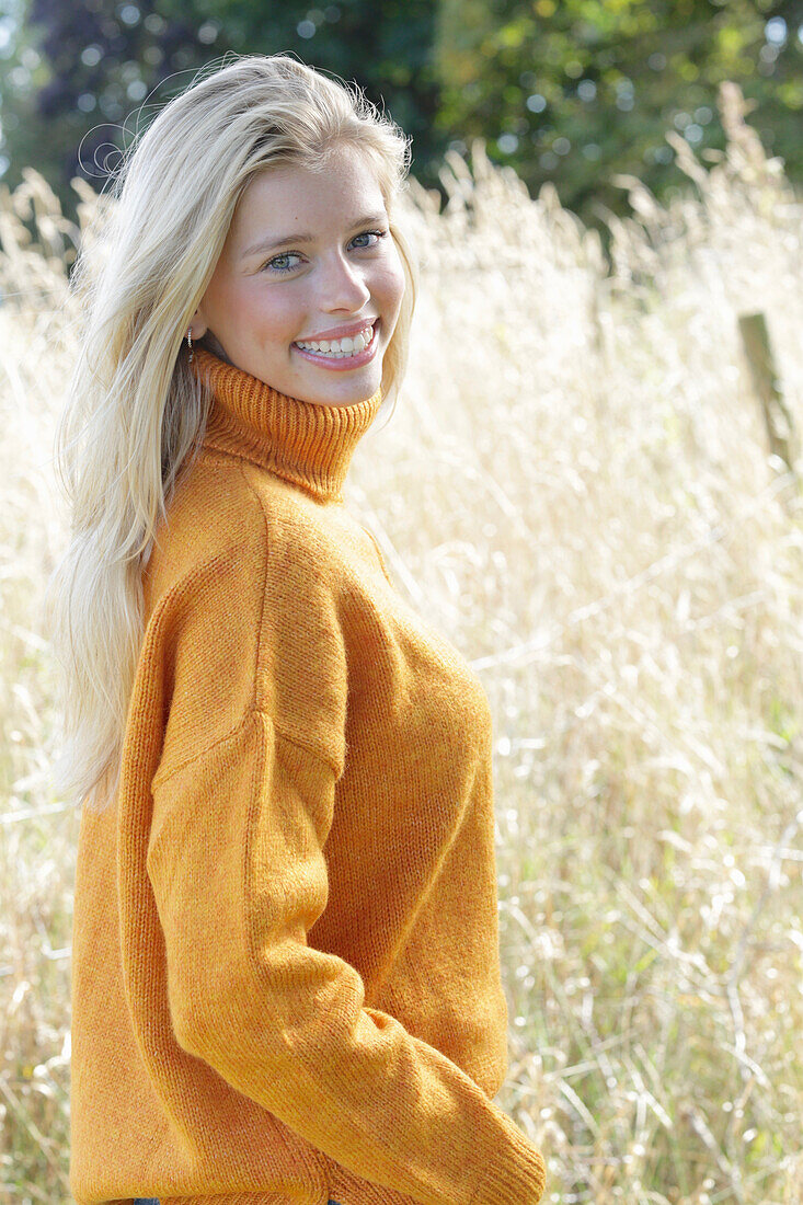 Junge blonde Frau in gelbem Rollkragenpullover in der Natur