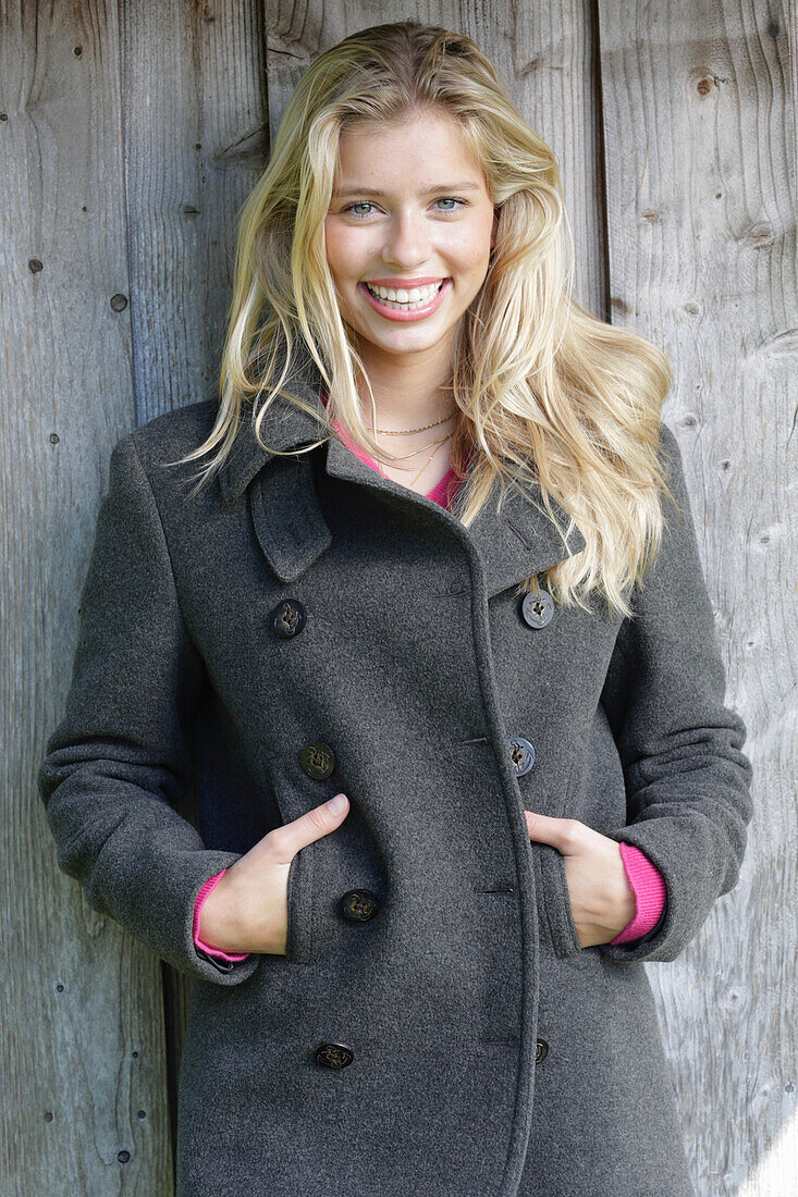 Young blond woman in a gray wool coat in front of a wooden wall
