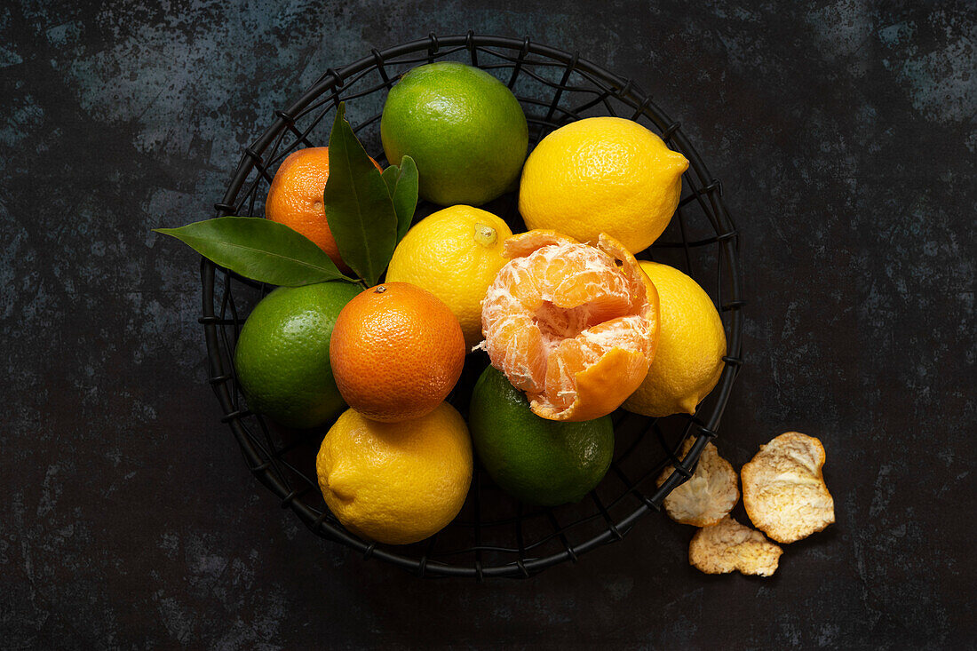 Lemons, limes and mandarins in a wire fruit basket, oOne mandarin is partially peeled