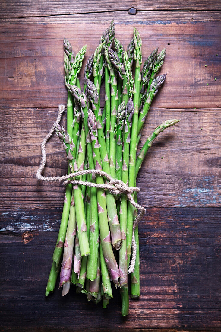 A bunch of freshly picked asparagus tied with string on a wooden background