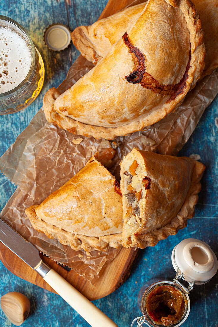 Several Cornish pasties on a wooden board served with pickled onions