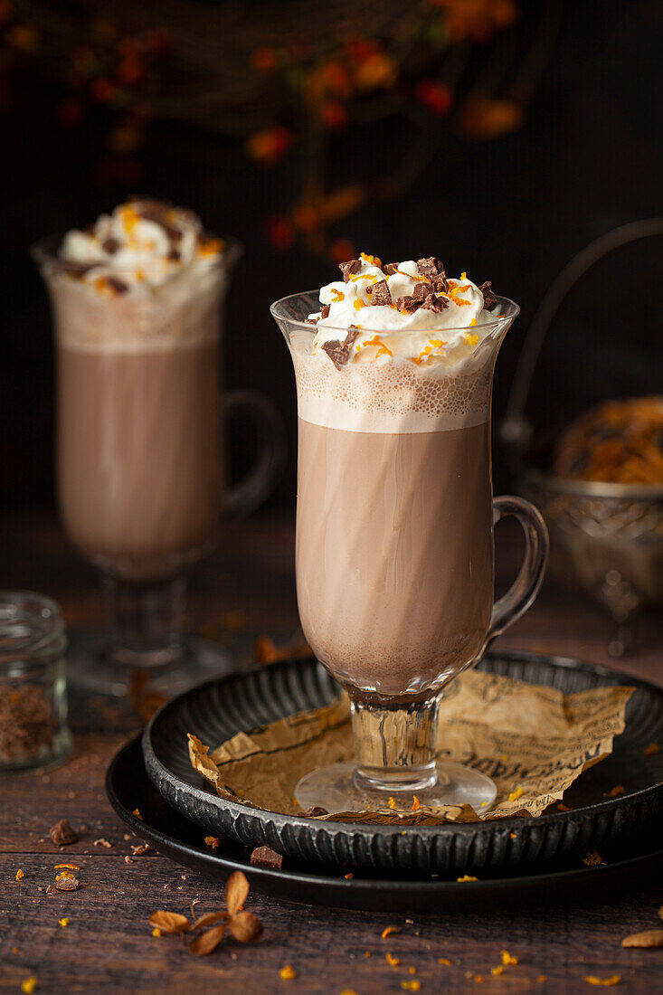 Two glasses of orange flavoured hot chocolate topped with whipped cream, orange zest and chocolate chunks