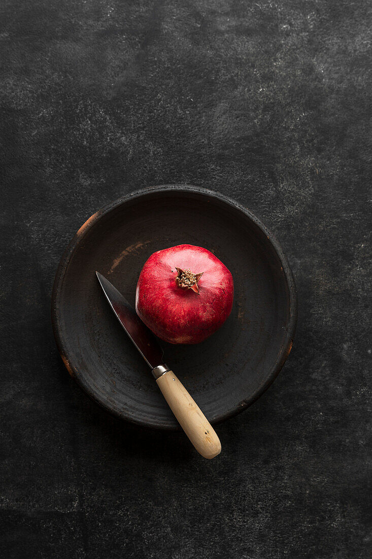Granatapfel mit Messer in schwarzer Keramikschale